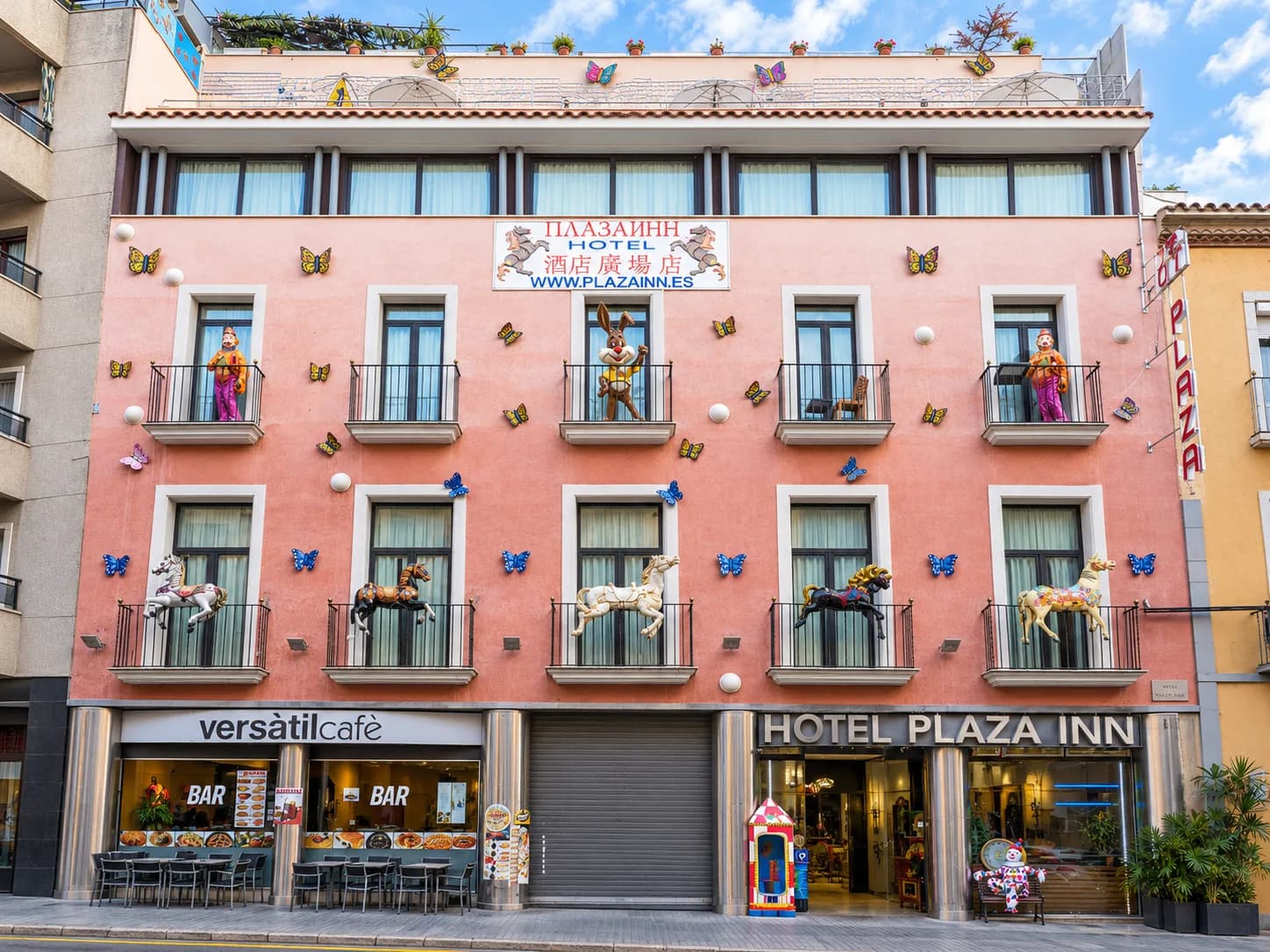 Fachada rosa del Hotel Plaza Inn en España con figuras decorativas y terraza del a pie de calle