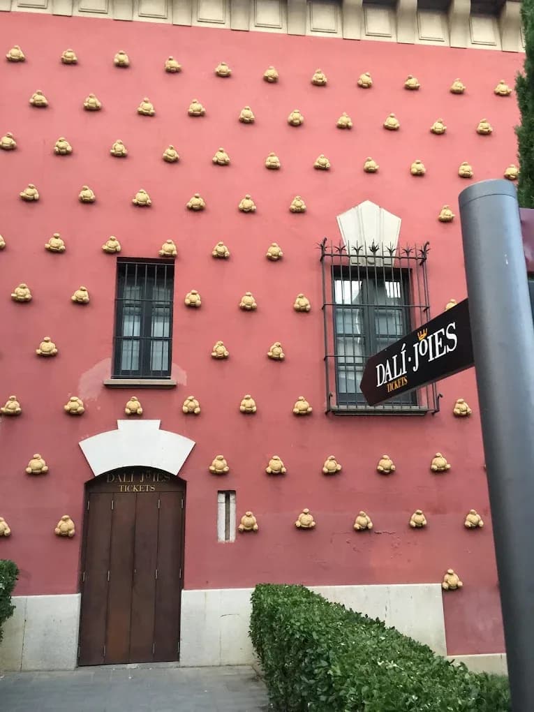 Fachada rosa decorada con relieves dorados y puerta de acceso junto a seto bajo cerca del Hotel Plaza Inn en Figueres, Spain