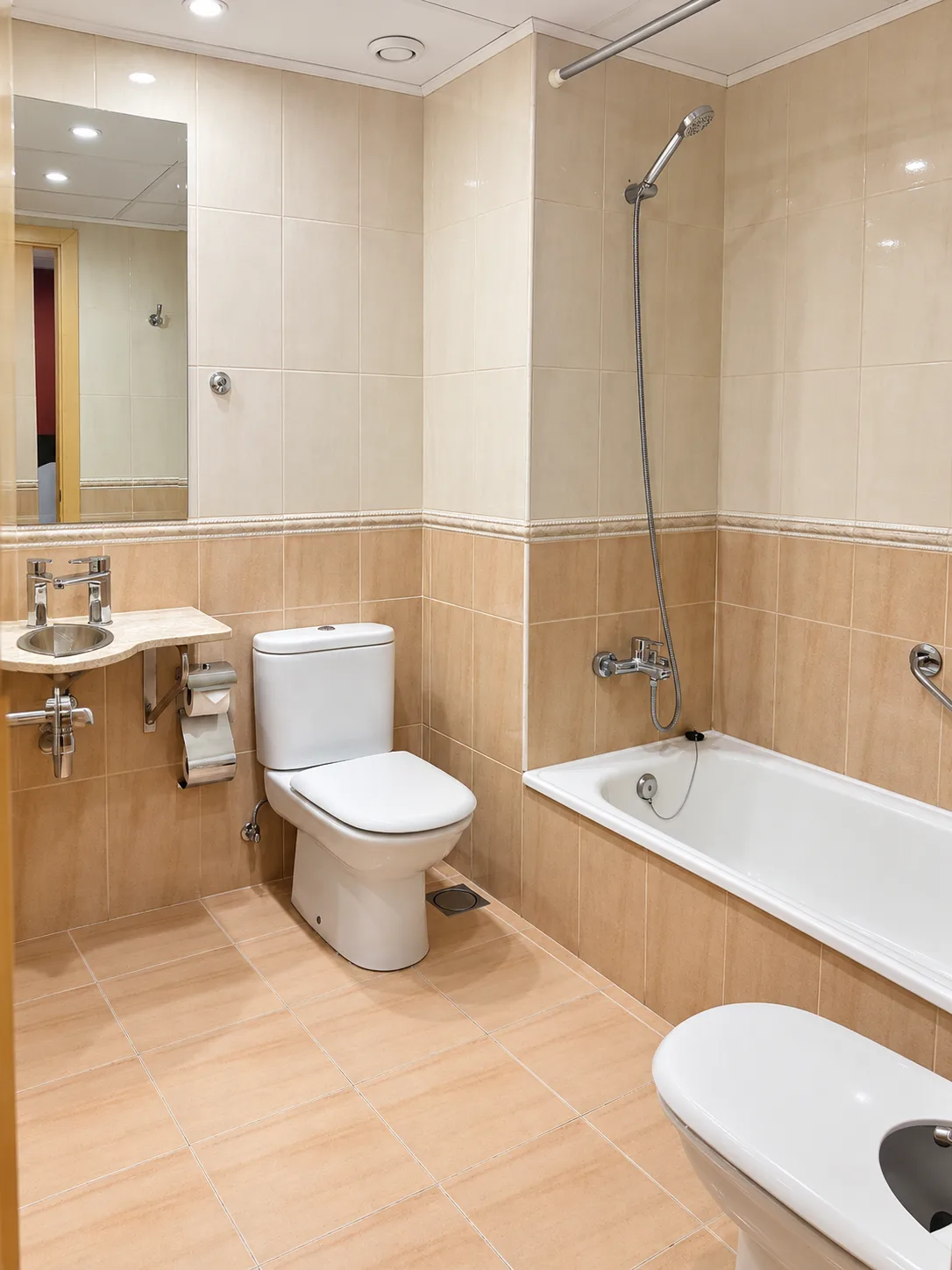 Baño privado de habitación en Hotel Plaza Inn Spain, con bañera, sanitario, bidé y lavabo sobre encimera en tonos beige claros